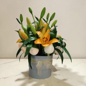 Bouquet of orange lilies and white roses with green leaves in a blue gift hatbox tied with a sheer ribbon.