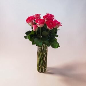 Bouquet of pink roses with green leaves in a tall clear glass vase on a soft, neutral background.