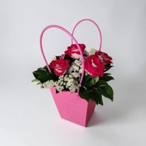 Pink gift bag holding a bouquet of pink roses and white filler flowers, against a light background.