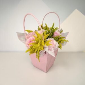 Pink gift bag filled with pink roses and bright yellow filler flowers, with tissue paper peeking out.