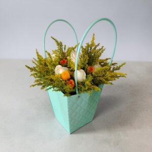 Turquoise woven basket with two handles holding a bright bouquet of yellow, orange, and white flowers on a gray surface.