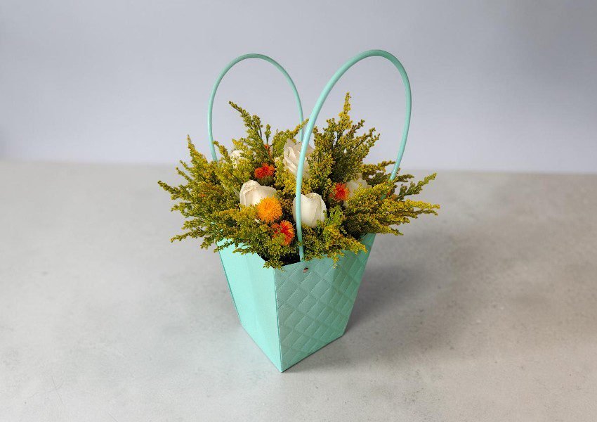 IMG_20260625_164001 2 | Elite Vibes - Jordan Turquoise woven basket with two handles holding a bright bouquet of yellow, orange, and white flowers on a gray surface.