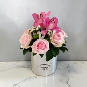 Pink roses and pink lilies in a white vase with green leaves on a marble countertop.
